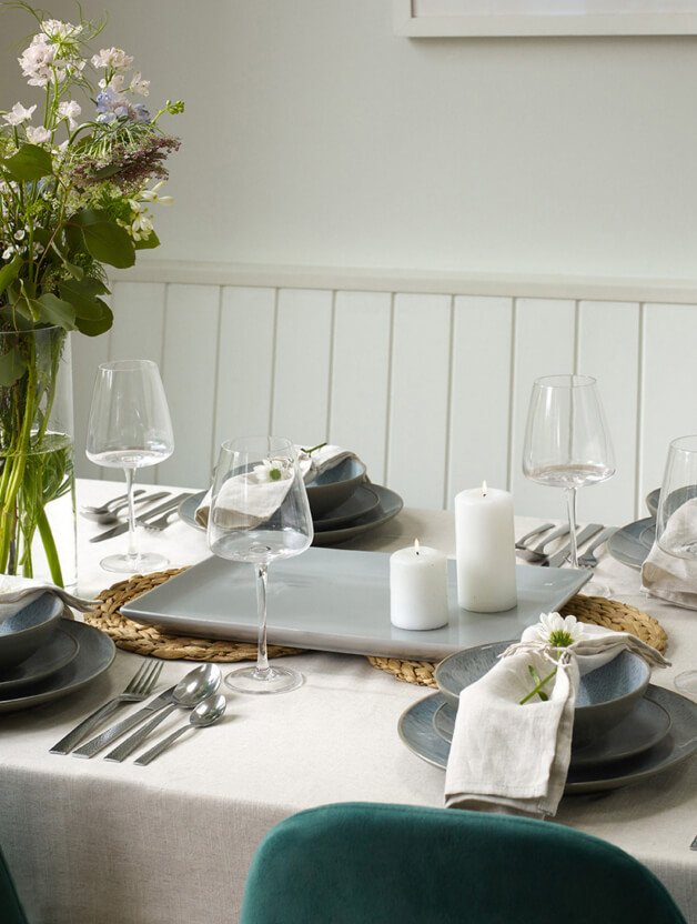 A dining table set with wine glasses, cutlery, grey crockery and white linens